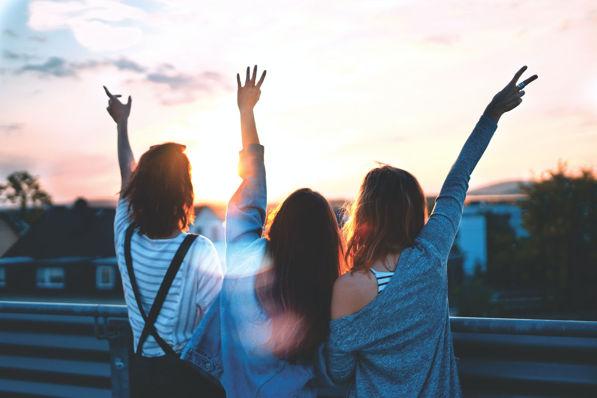 Three girls captured from the back raising their hands up and watching sunset 
